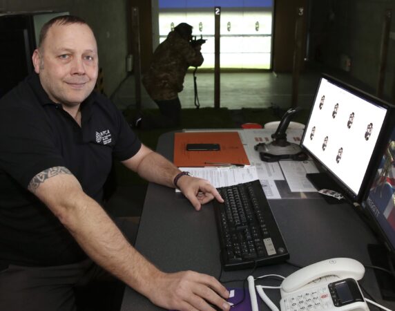 Man at computer with shooting range in background