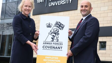 Woman and man holding a Gold Award banner outside York St John University