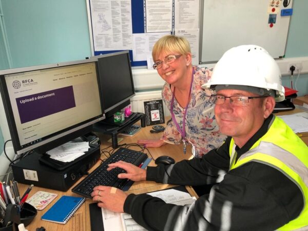 Man in hard hat in front of computer with smiling woman