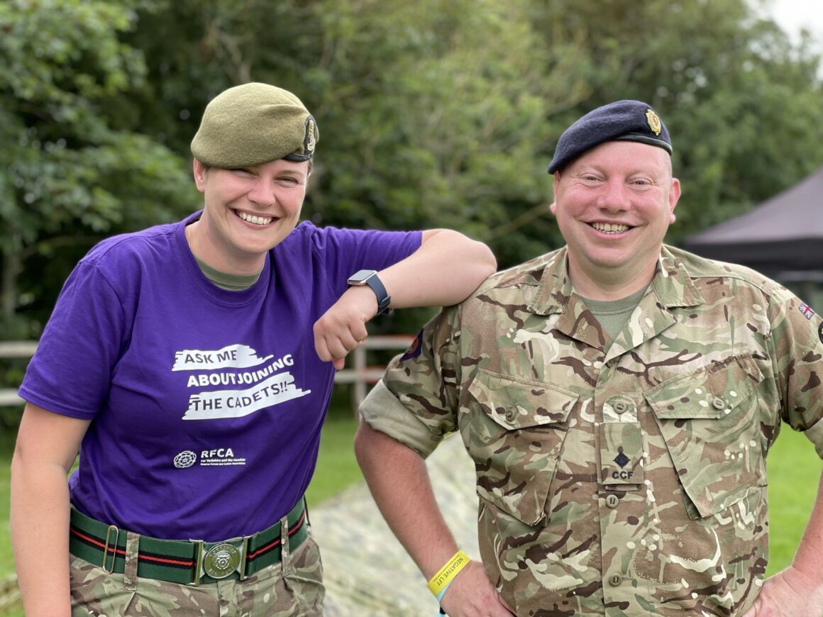 Two cadet force adult volunteers , one wearing a bright purple t-shirt promoting the cadets