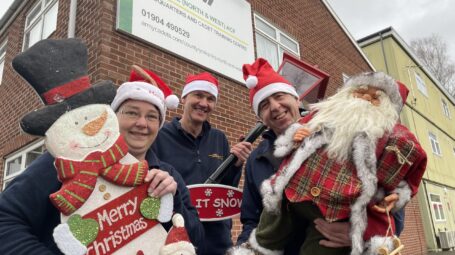 Three people in santa hats and holding Christmas decorations